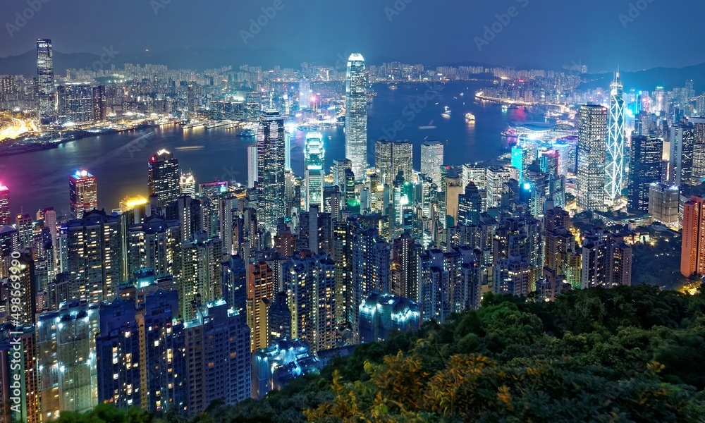 Night scenery of Hong Kong viewed from Victoria Peak with city skyline of crowded skyscrapers by Victoria Harbour and Kowloon area across seaport ~ Beautiful cityscape of Hong Kong in blue twilight