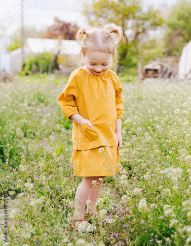 little girl with pigtails in yellow dress standing in field of flowers photo