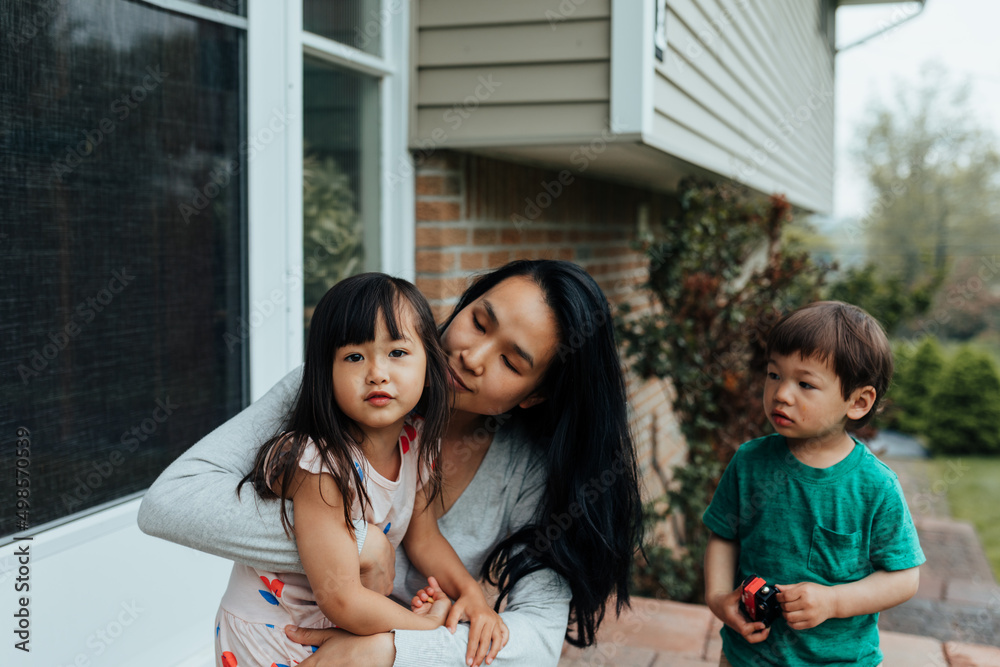 Mother sitting on front porch with daughter in her lap and son nearby Mother sitting on front porch with daughter in her lap and son nearby