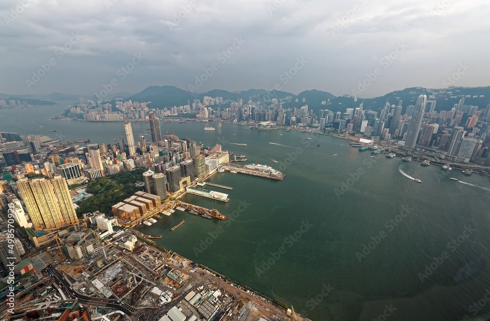 Aerial view of Hong Kong & Kowloon ( Tsim Sha Tsui ) on a gloomy cloudy day with city skyline of crowded skyscrapers by Victoria Harbour & ships across the busy seaport~Beautiful cityscape of Hongkong