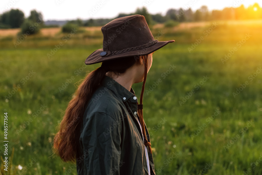 Obraz premium Defocus young woman in cowboy hat. Girl in a cowboy hat in a field. Sunset. Nature background. Woman looking in the direction of the sun. Hope, future. Out of focus