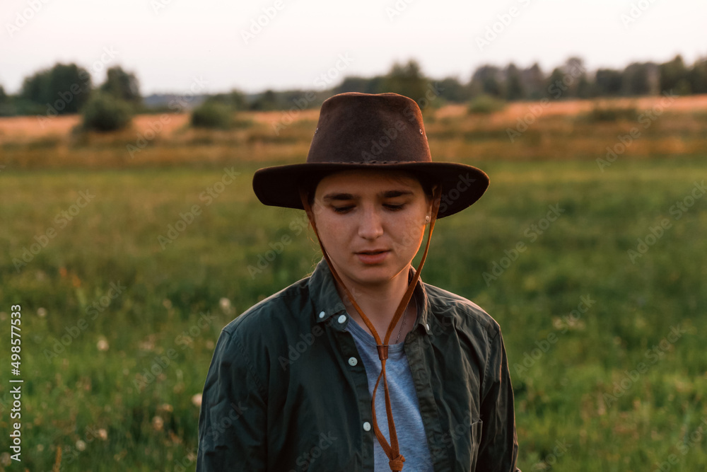 Defocus young woman in cowboy hat. Girl in a cowboy hat in a field. Sunset. Nature background. Closeup portrait caucasian girl. Summertime. Fashion. Out of focus