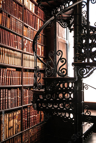 Vertical shot of a spiraling staircase near a shelf of vintage books