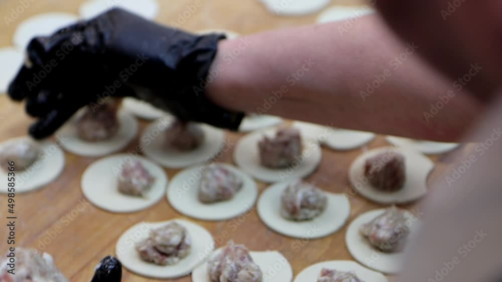 The cook is putting meatballs in dough for making dumplings. Professional cooker works fast at grocery store, close-up hands 4k footage The cook is putting meatballs in dough for making dumplings. Professional cooker works fast at grocery store, close-up hands 4k footage