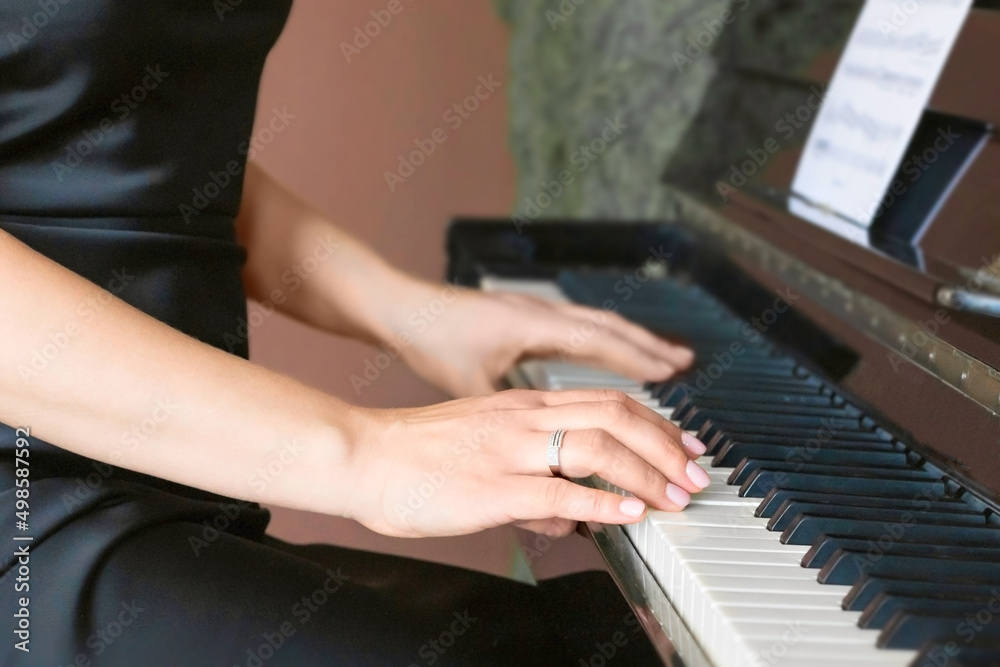 Obraz premium Selective focuse of hand of an adult woman with a beautiful manicure against the background of black and white keys of a classical piano. The concept of creative activities, hobbies.
