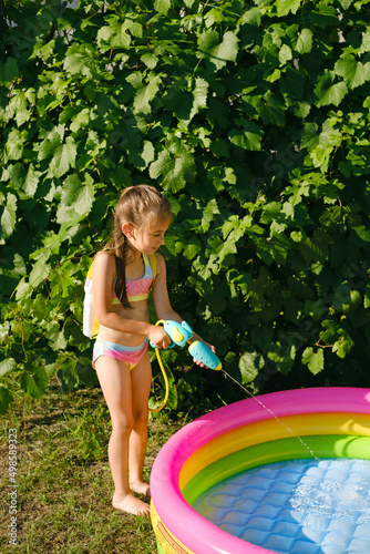 Konstfotografi Child plays with a water blaster, into which water enters through a tube from a backpack with a container