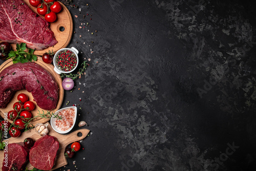 Variety of fresh raw beef steak with spices for grilling on a dark background. Whole piece of steaks ready to cook. banner, menu, recipe place for text, top view