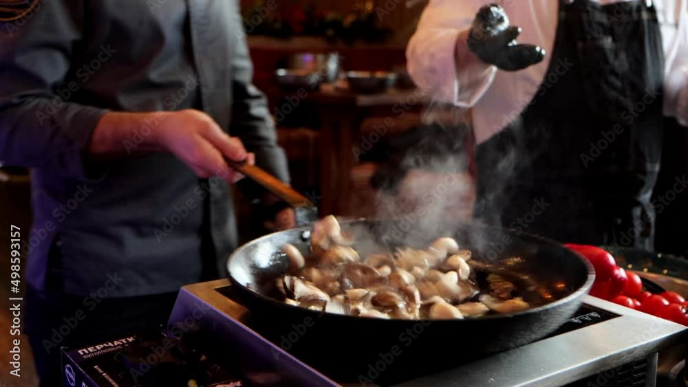 Two unrecognizable chefs are preparing food at cooking class. Cook salts mushrooms in cooking pan and mixing it, close-up 4k video Two unrecognizable chefs are preparing food at cooking class. Cook salts mushrooms in cooking pan and mixing it, close-up 4k video