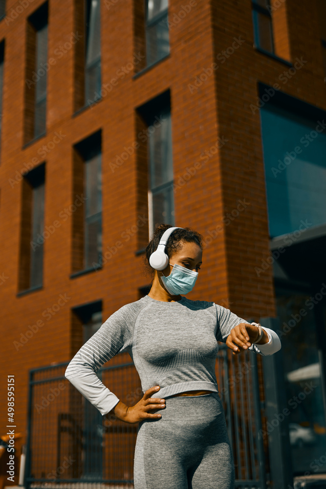 Woman in light gray sportswear and medical mask having a break during training on the street