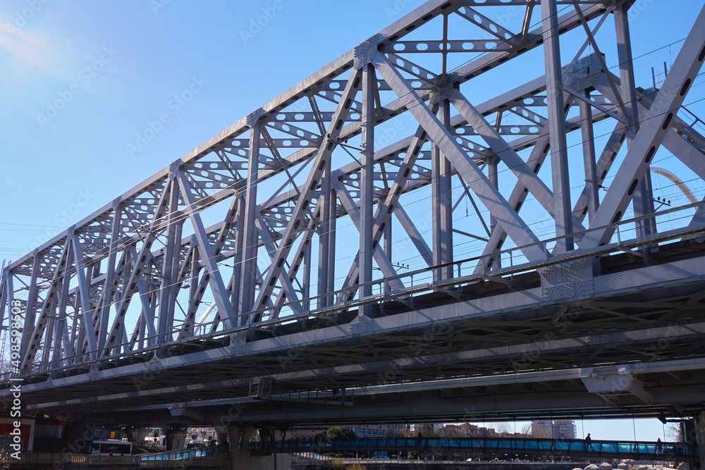 Steel structures of the railway bridge. The railroad runs through the center of the city. View of the blue cloudless sky.
