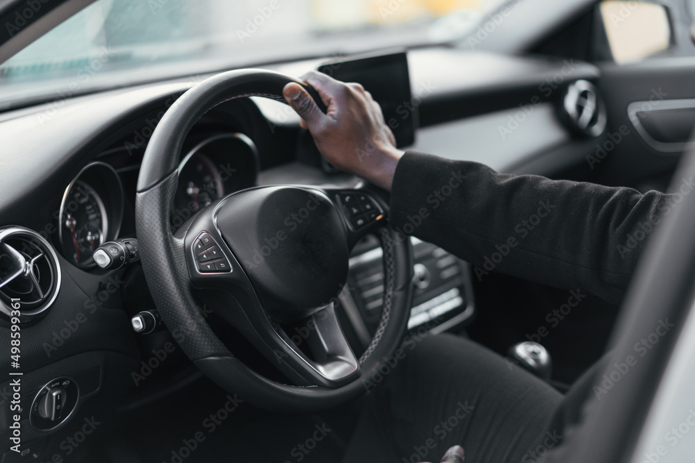 photo of the hand of an African American businessman in a suit touching the steering wheel of a car