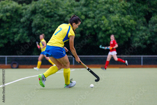 Young female field hockey player lead the ball in attack at heavy rain