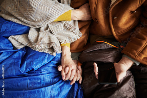 Close up of adult refugee couple holding hands hiding in shelter during war or crisis  copy space