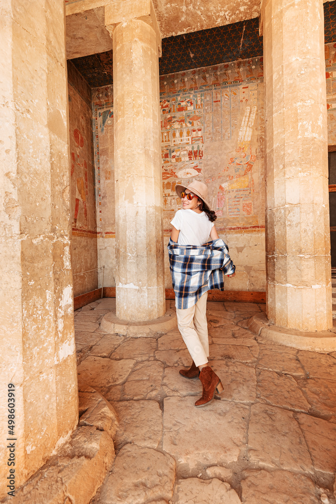 Happy woman traveler explores the ruins of the ancient egyptian Hatshepsut temple in the heritage city of Luxor. Columns with painted hieroglyph and carvings