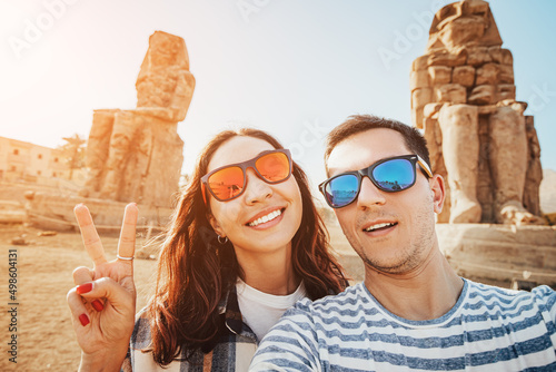 Happy traveler couple in love takes a selfie photo near the famous colossi of Memnon pharaoh statues in Luxor during the honeymoon tour in Egypt
