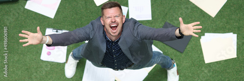 Man in suit throwing papers on green grass and yelling with his hands up top view photo