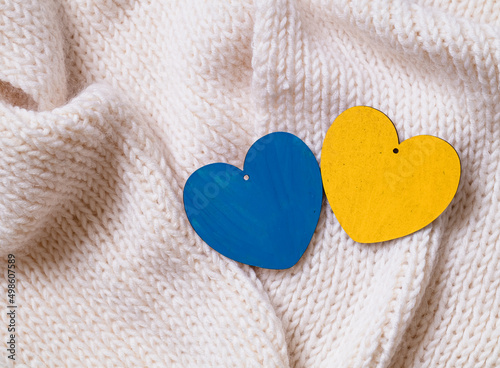 The concept of ending the war in Ukraine. Two wooden hearts with colors of the national flag of Ukraine. Blue and yellow hearts on a white knitted fabric.