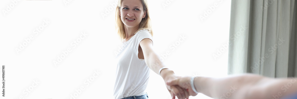 Young woman holding man hand near window at home Young woman holding man hand near window at home