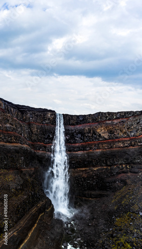 Hengifoss waterfall with deep red layers under cloudy sky