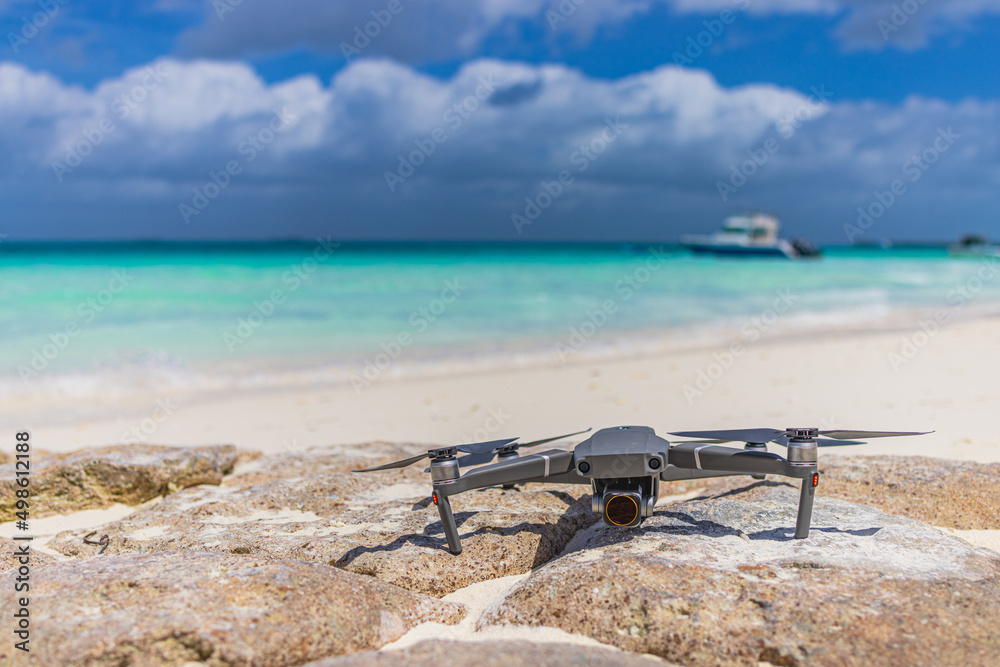 Drone landed on rocks surface next to seashore. Blurred tropical beach shore, coastline landscape, boats and cloudy sky. Luxury filming, footage and content creating for tourism, advertising