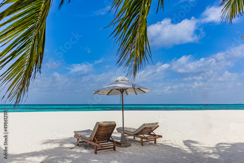 Beautiful tropical island scenery  two sun beds  loungers  umbrella under palm tree. White sand  sea view with horizon  idyllic blue sky  calmness and relaxation. Inspirational beach resort hotel 