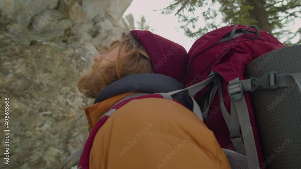 Low angle shot of bearded male tourist standing in mountains and looking up while hiking in winter