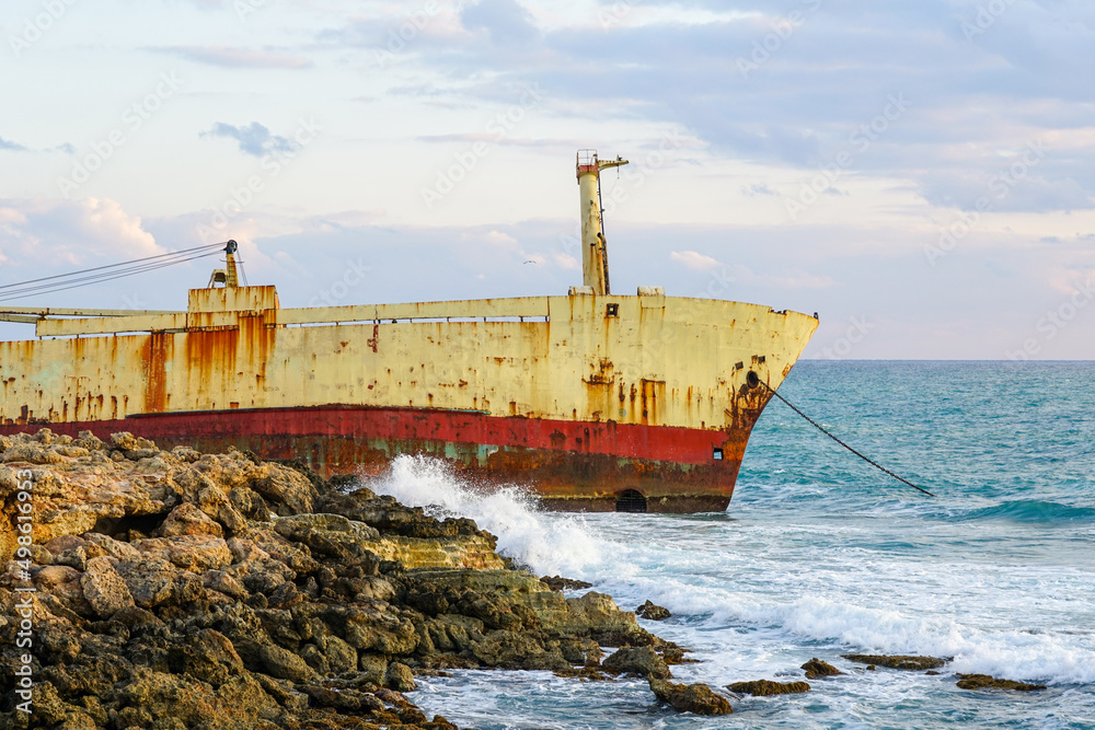 a large rusty shipwreck on a rocky coast against a blue sky background