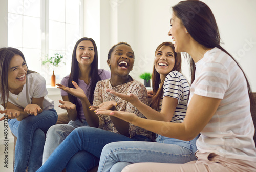 Overjoyed millennial diverse multiethnic girlfriends rest at home have fun indoors together. Smiling happy gen z multiracial girls laugh joke enjoy time chatting. Diversity, friendship concept.