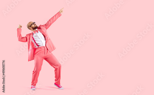 Fotografie Cheerful successful man dancing funny making movements winner isolated on pink background