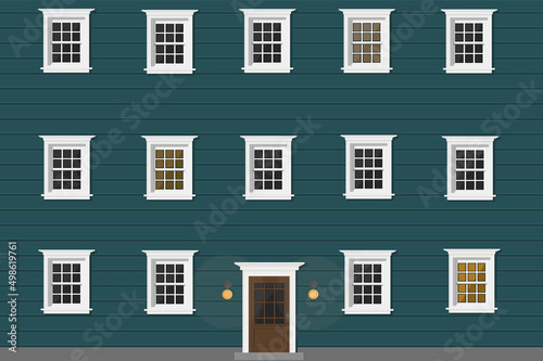 a big blue wooden house with white windows and white door and light in windows in the evening