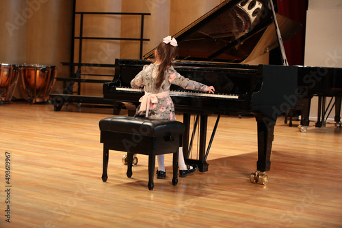 Child young artist behind a big black grand piano playing on the stage of a concert hall general view of a musical event