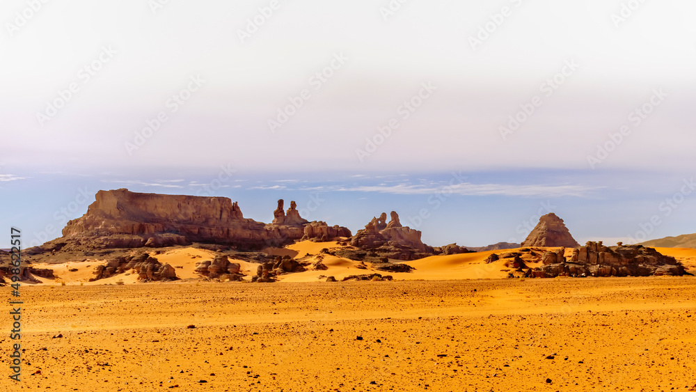 Tadrart Rouge, Djanet, Illizi. Orange color reg stones, sandstones. Blue covered sky. Panoramic view of Sahara Desert sand dune and rocky mountains with awesome human shapes like a family sitting down