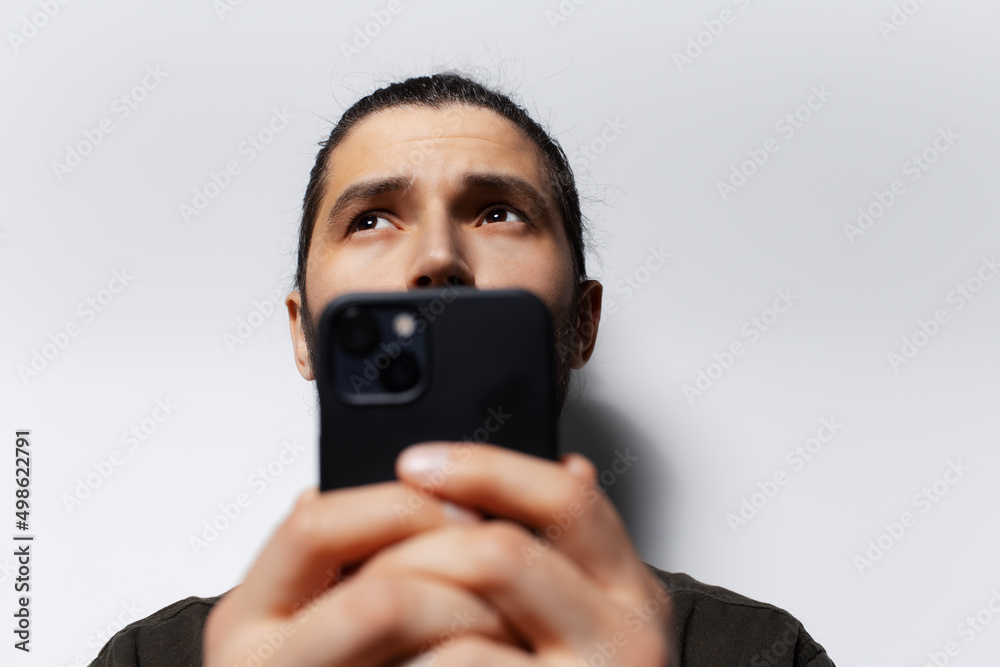Close-up portrait of thoughtful man with smartphone in hands, looking up.