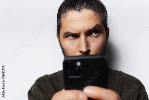 Close-up portrait of young man with smartphone in hands, looking up, on white. © Lalandrew