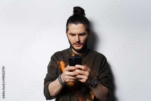 Portrait of young man with hair bun, looking in smartphone on white background.