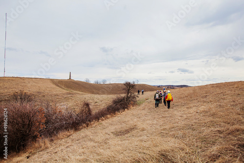 Group of hikers with backpacks walking on a rural trail. Countryside nature landscape. Active people outdoor. Healthy lifestyle activity. Pasture Area. Cloudy spring day. Back view. 