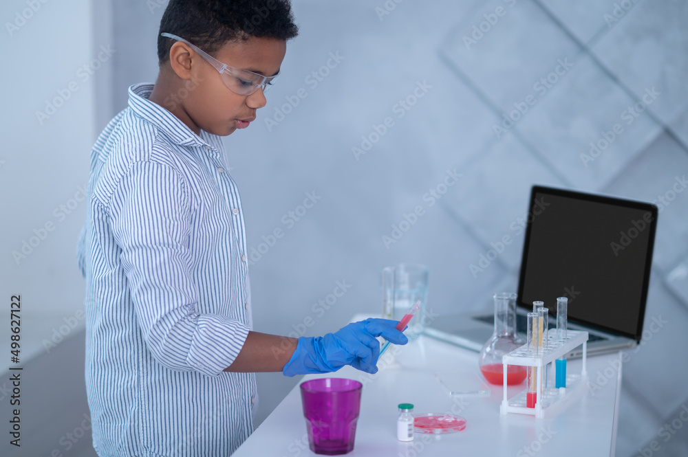 A boy in a lab coat working with test tubes and looking involved A boy in a lab coat working with test tubes and looking involved