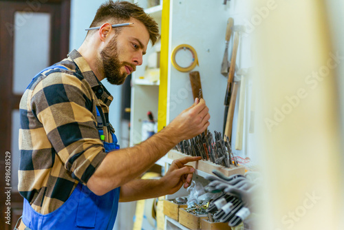 Bearded caucasian carpenter checking and measures drills photo