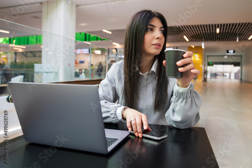 A young woman drinks coffee while working at a laptop in a cafe
