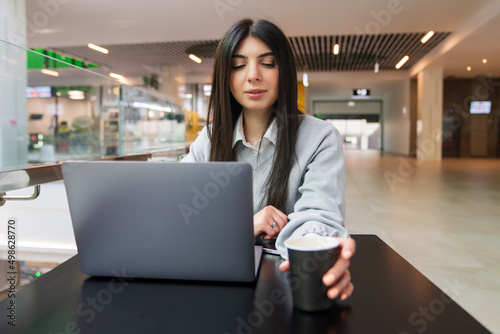 A young woman drinks coffee while working at a laptop