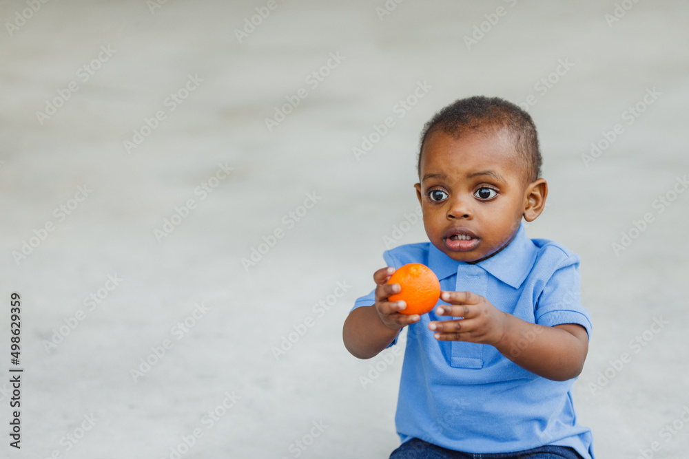 A cute one year old toddler almost preschool age African-American boy holding a healthy snack of an orange A cute one year old toddler almost preschool age African-American boy holding a healthy snack of an orange