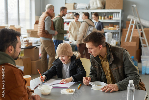 Portrait of Caucasian father and son enjoying simple meal at soup kitchen or help center for refugees, copy space photo