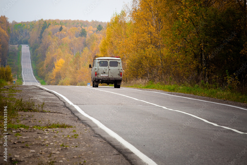 An old car rides along asphalt road in the autumn forest