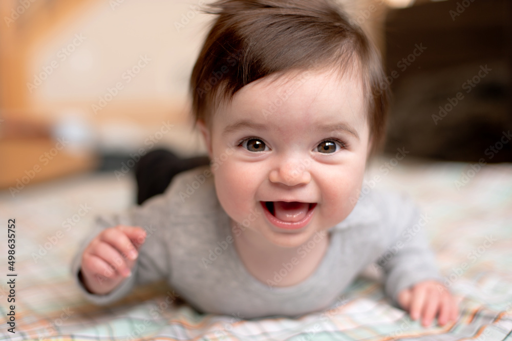 A baby is laying on their stomach and smiling at the camera A baby is laying on their stomach and smiling at the camera
