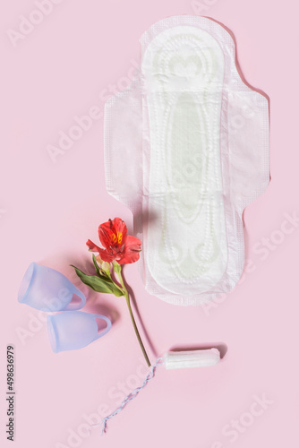 Menstrual hygiene products, including a cup, pads and a tampon on a pink background top view.