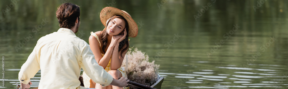 dreamy woman in straw hat looking at romantic boyfriend during boat ride, banner.