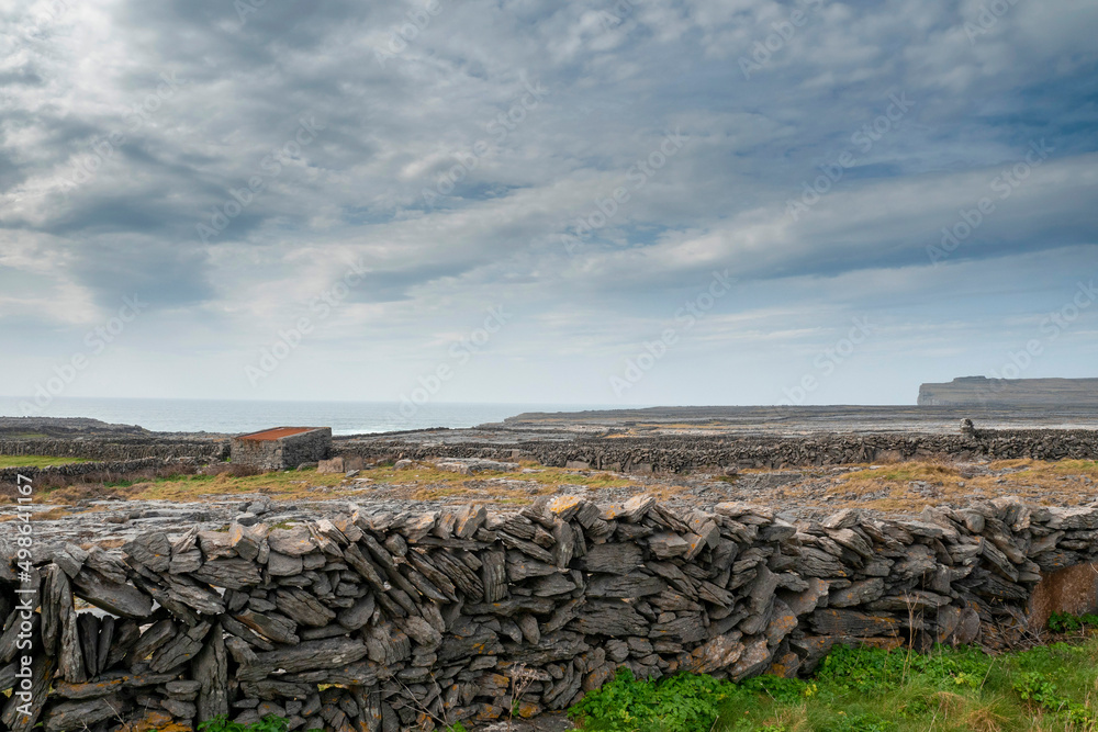 Nature scene of Inishmore,, Aran island. Rough stone terrain. Blue cloudy sky. Maze of dry stone walls and small shed with red metal roof Popular tourist area with amazing nature view.