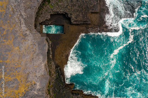 Aerial view on Poll na bPéist Wormhole, Inishmore, Aran Island. Ireland. Famous and popular tourist landmark. Natural basin in rough stone coast filled with ocean water. Blue ocean water. photo