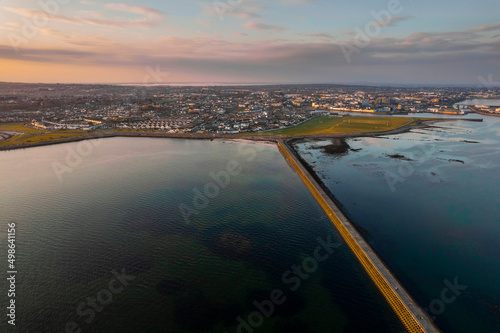 Causeway to Mutton island and Galway bay, town center in the background, Cloudy sky. Ireland. Blue ocean water at sunset. Irish landscape. Aerial view © mark_gusev