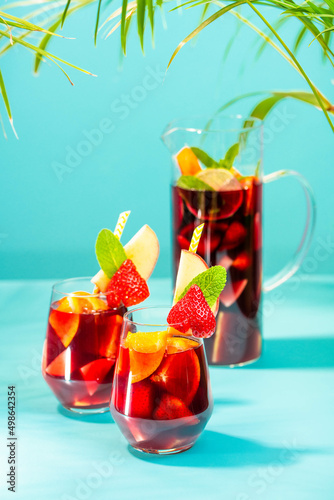 A pitcher filled with summer spanish cocktail sangria and glasses decorated with a pice of apple, strawberry and a pinch of mint.